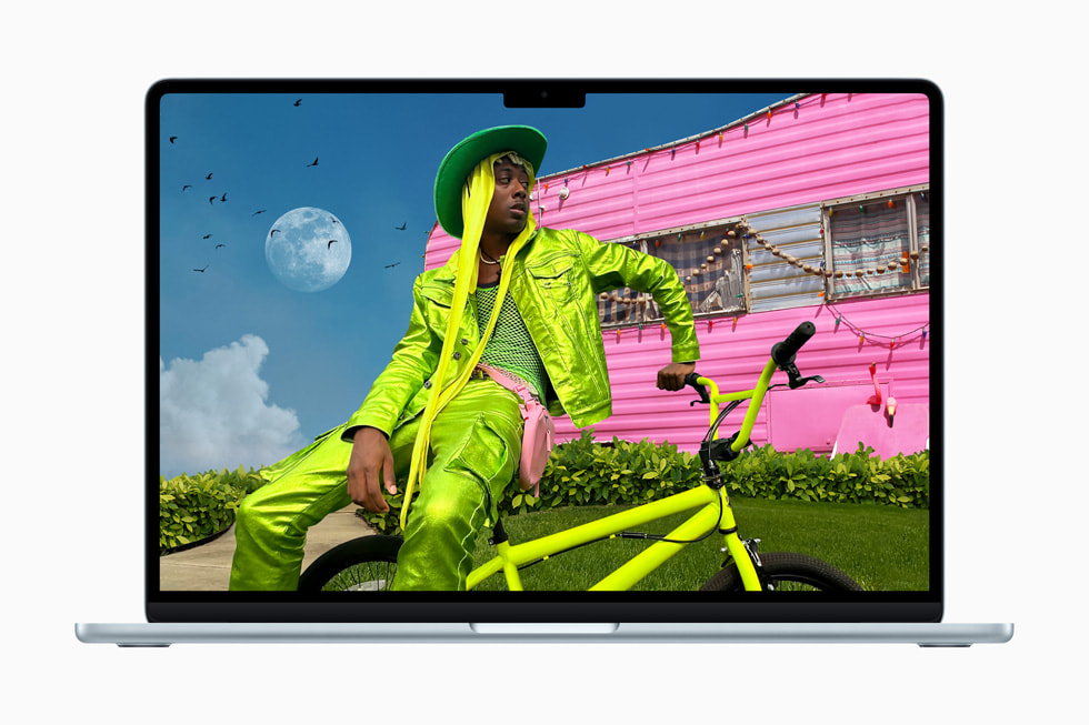 Un MacBook Air affichant une photo stylisée d’une personne habillée en vert fluo, assise sur un vélo assorti, devant un camping-car rose fluo. 