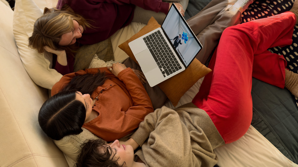 Trois personnes assises sur un canapé regardent la série Severance sur un MacBook Air.