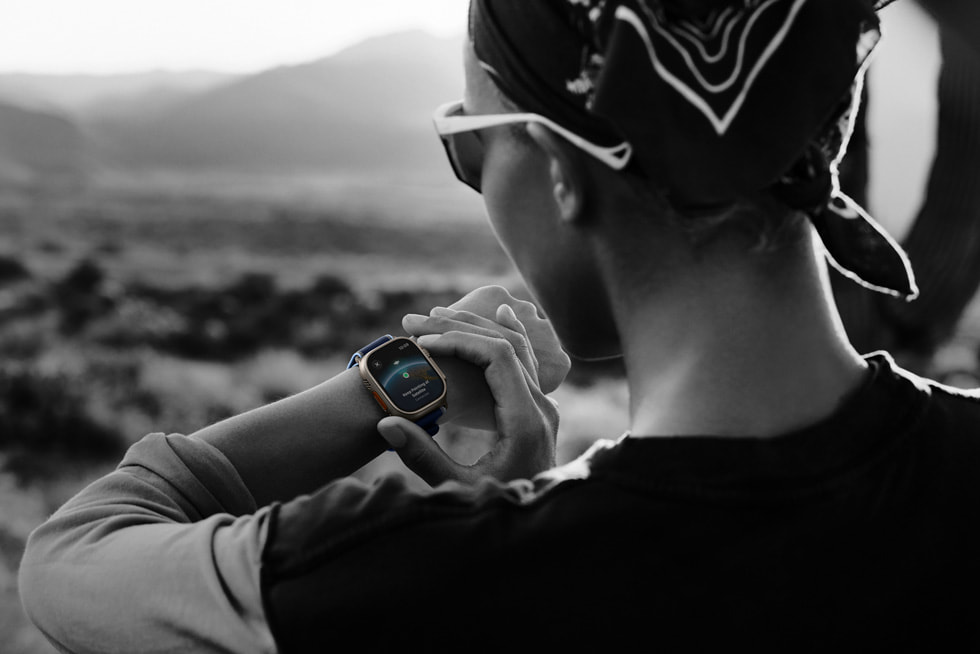 Une photo en noir et blanc d’une personne qui court dans un désert en vérifiant sa connexion par satellite sur l’Apple Watch Ultra 3.