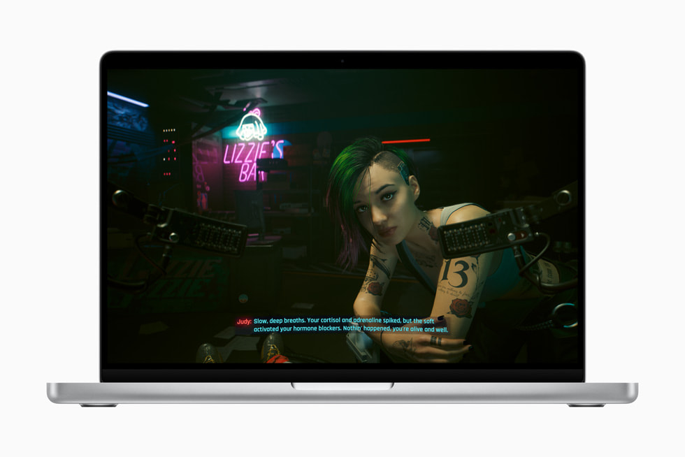 Captura de pantalla de Cyberpunk 2077 que muestra a un personaje con tatuajes llamada Judy sentada fuera del Lizzie’s Bar. Le dice al jugador, en inglés: "Respira profundo. Se te dispararon los niveles de cortisol y adrenalina, pero el software activó tus bloqueadores de hormonas. Así que todo bien. Estás a salvo".