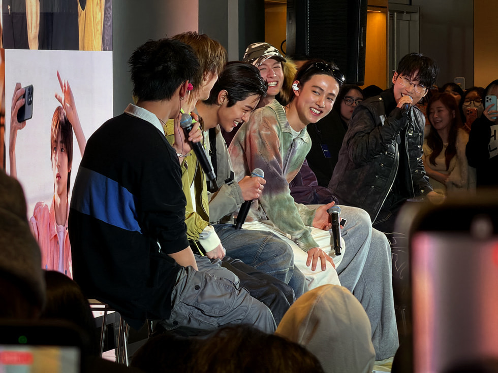 The members of the band CORTIS are pictured smiling and sitting with microphones in their hands at Apple Myeongdong in Seoul.