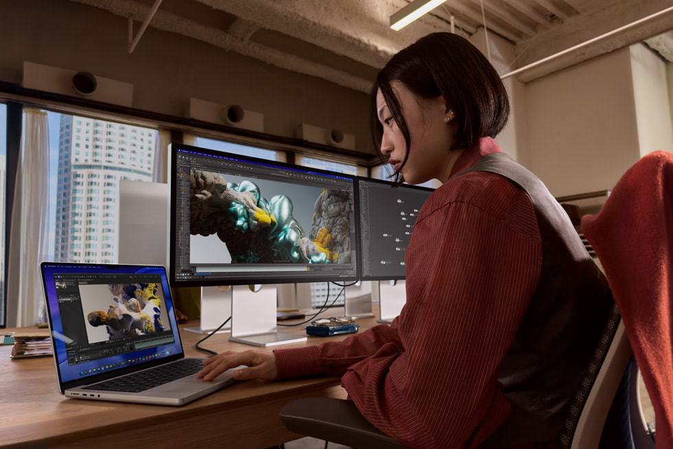 A person uses Studio Display XDR and MacBook Pro in an office-like setting.