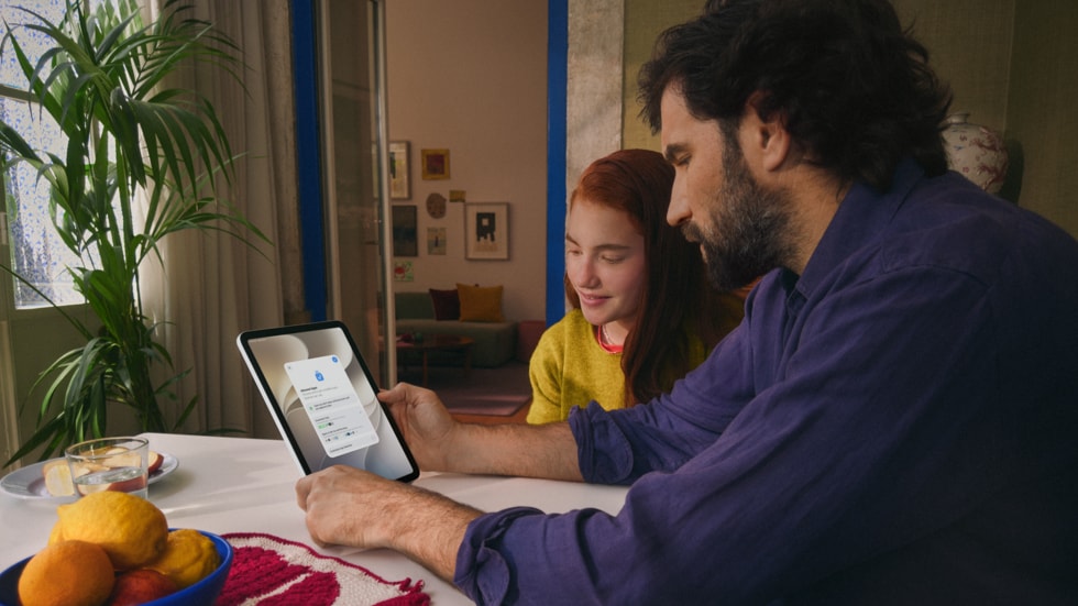 A person and a child sit together at a wooden table, interacting with iPad.