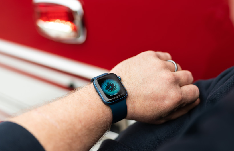 Een arm met een Apple Watch geeft het bericht weer: Nu inademen, met een brandweerwagen in de buurt