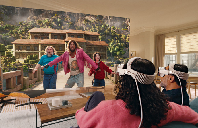 Zwei Personen, die beide eine Apple Vision Pro tragen, sitzen nebeneinander auf der Couch und schauen „Ein Minecraft Film“, wobei sich der Bildschirm über den gesamten Raum erstreckt