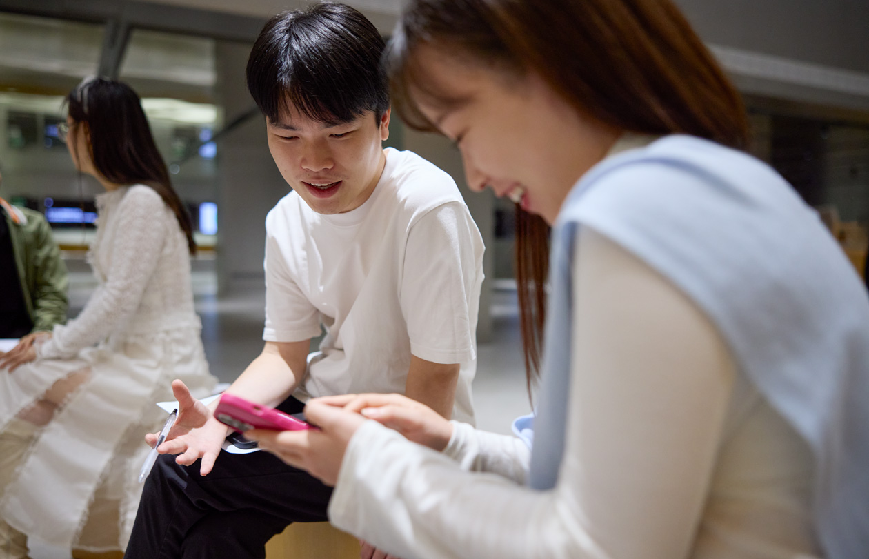 Two people talk as they look down at an iPhone that one of them holds and navigates