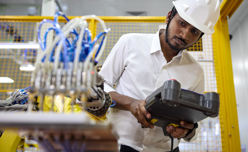 A robotics employee holds a work device as they peer at a robotics machine